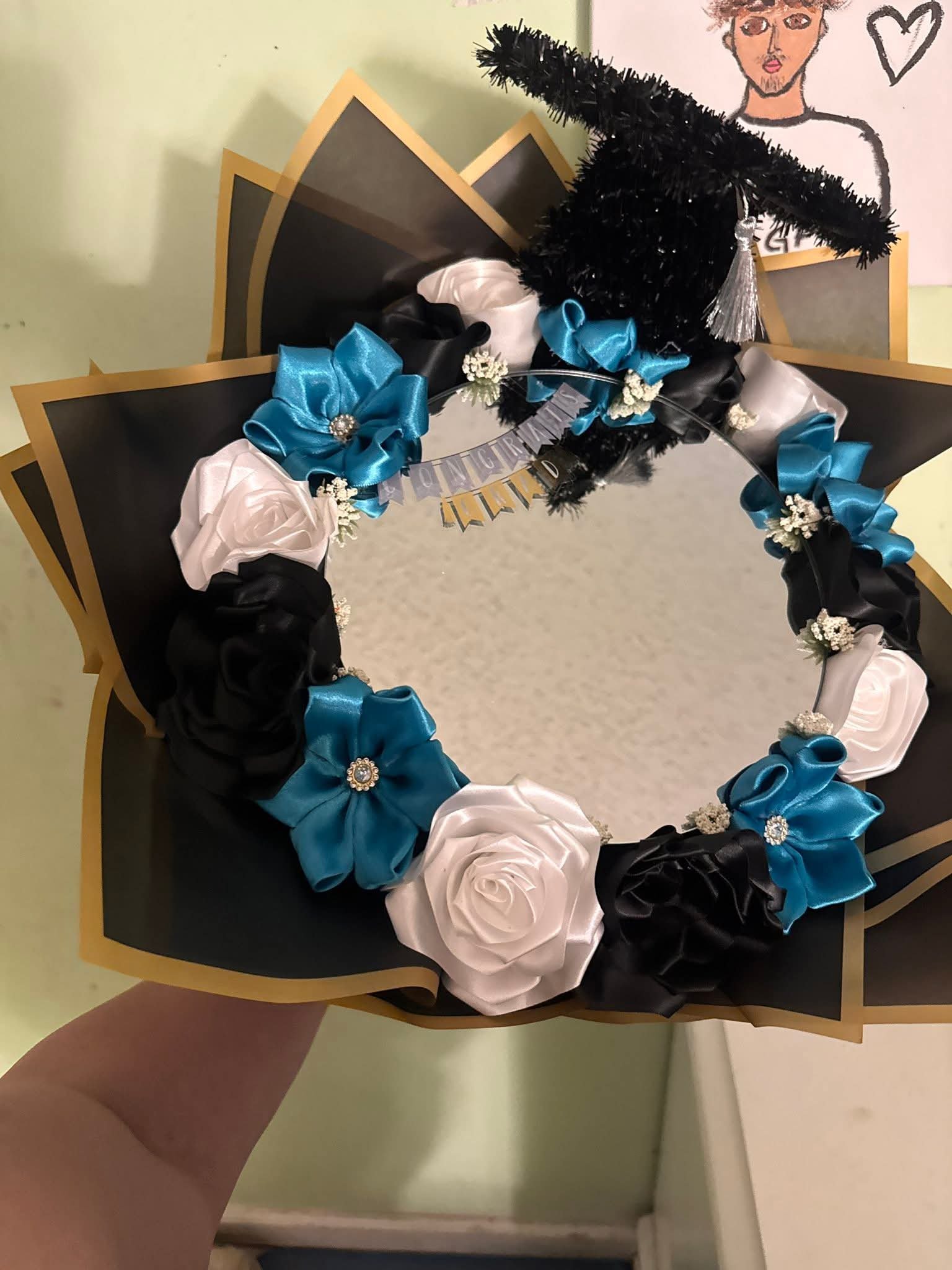 Graduation wreath bouquet with black, white and teal ribbon roses around a mirror and mini graduation cap